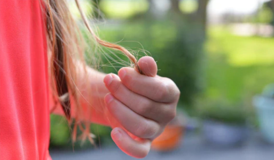 A woman with brown blonde thinning hair pulling at her hair. Concept of hair loss mistakes, hair mistakes to avoid for thinning hair.