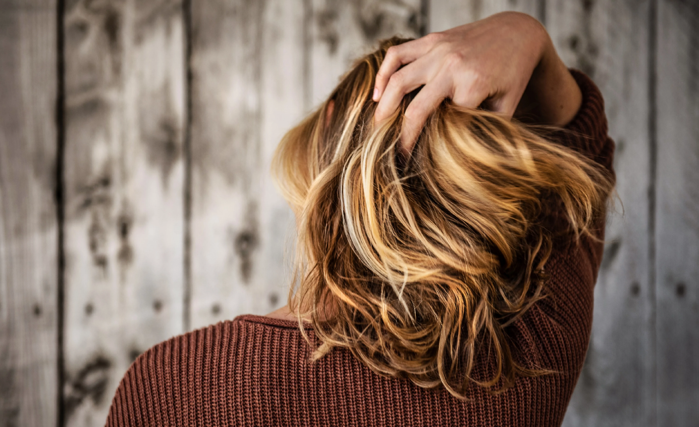 A stressed woman seen from the back, holding her blonde hair. Concept of stress, hair loss, types of hair loss.